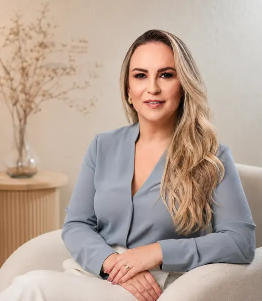 Retrato da Dra. Luana Arivabeni, de blusa azul, sentada no consultório